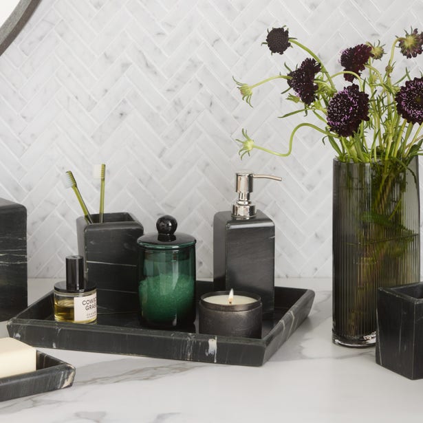 Dark green glass bath canister on black marble tray, styled with bathroom accessories and florals.