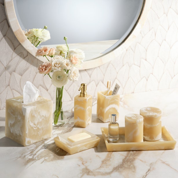 Honey alabaster-toned bath accessories set styled on marble vanity with floral arrangement.
