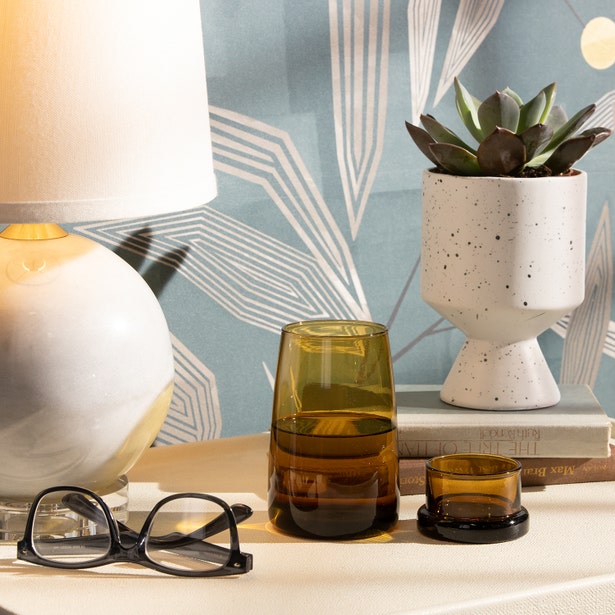 Amber glass carafe and tumbler styled on a nightstand with lamp, succulent, and eyeglasses.
