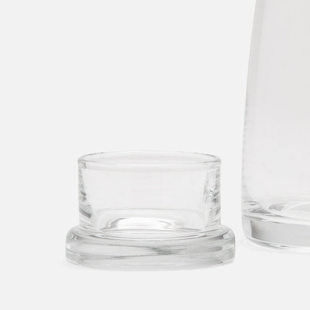 Close-up of clear glass carafe lid resting beside the vessel on a white surface.