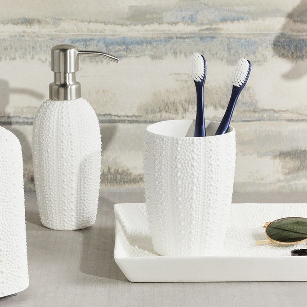 White textured bath accessories set styled on a vanity with watercolor wallpaper backdrop.