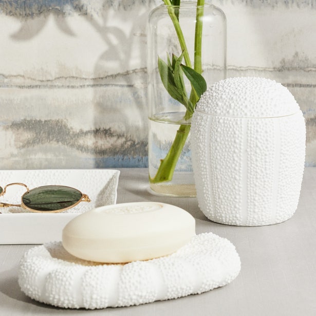 Textured white ceramic soap dish with bar soap alongside matching Hilo bath canister, bamboo stems in background.