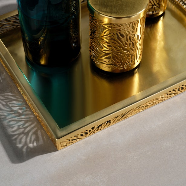 Close-up of ornate gold tray edge with teal glass soap pump and gold vessel on linen surface.