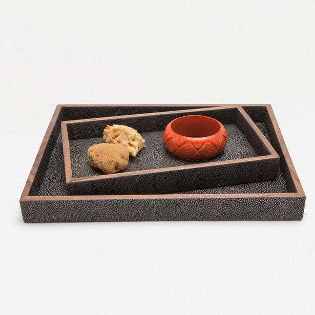 Two dark charcoal shagreen-textured nesting trays with copper trim, styled with a coral bowl and sponge.