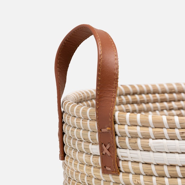 Close-up of tan leather handle with cross-stitch detail on woven seagrass hamper.