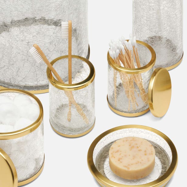 Crackle glass bath canisters with gold rims, styled with toothbrush, cotton swabs, and soap.