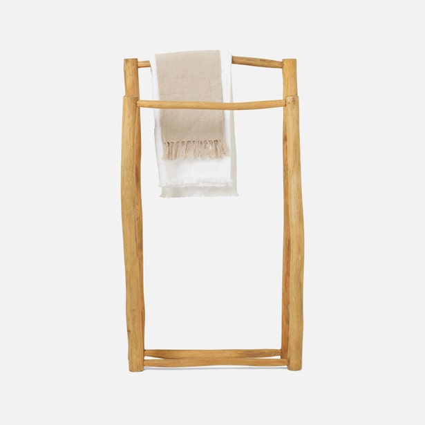 Natural teak freestanding towel rack with draped fringed linen towel in sand.