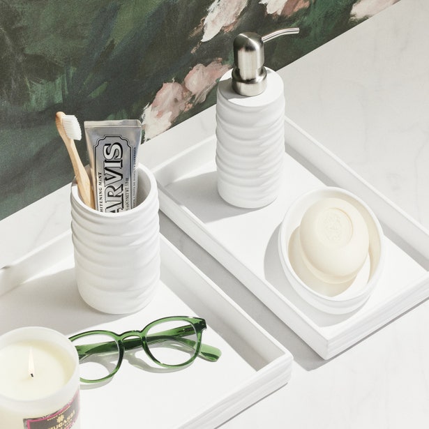 White ribbed bath canister styled on tray with soap dispenser and soap dish in bathroom vignette.