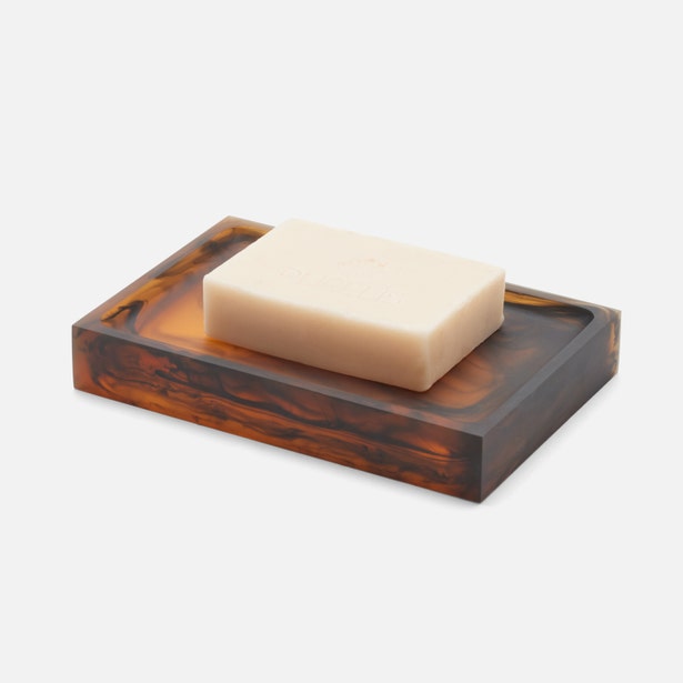 Tortoiseshell resin soap dish holding an ivory bar of soap, angled three-quarter view.