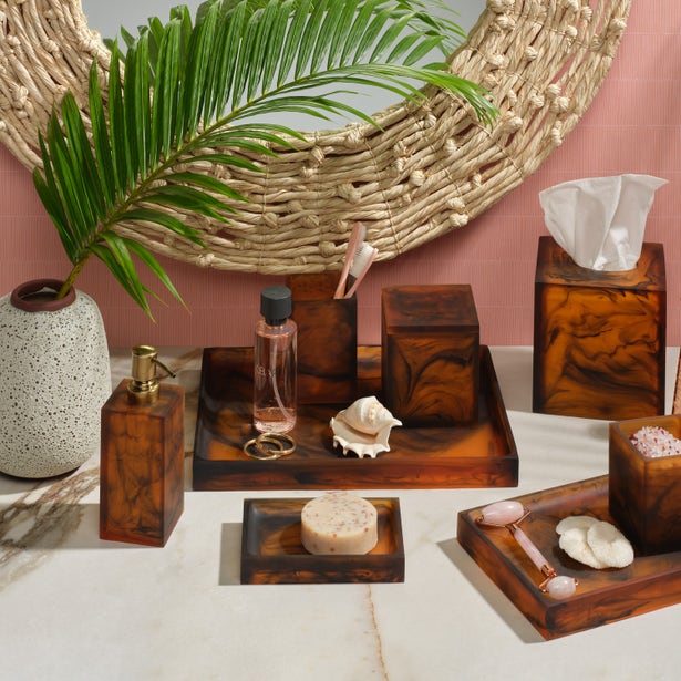 Tortoiseshell resin bath accessories collection styled on marble vanity with palm leaf and woven mirror.