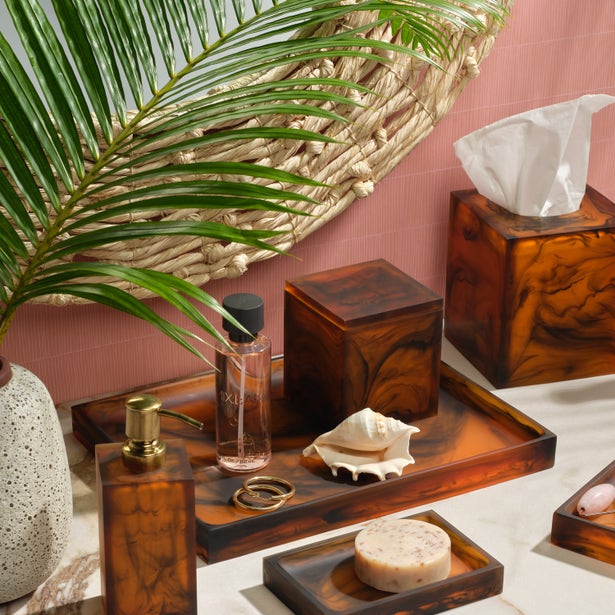 Tortoiseshell resin bath accessories styled on a pink linen backdrop with palm fronds.