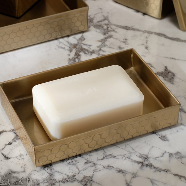 Gold honeycomb-embossed soap dish holding an ivory bar soap on marble surface.