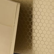 Corner detail of Temara brush holder against hexagonal tile wall, champagne finish.