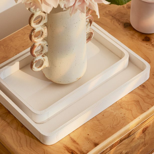 Two ivory textured trays nested on a wood surface, styled with a ceramic vase and pink flowers.