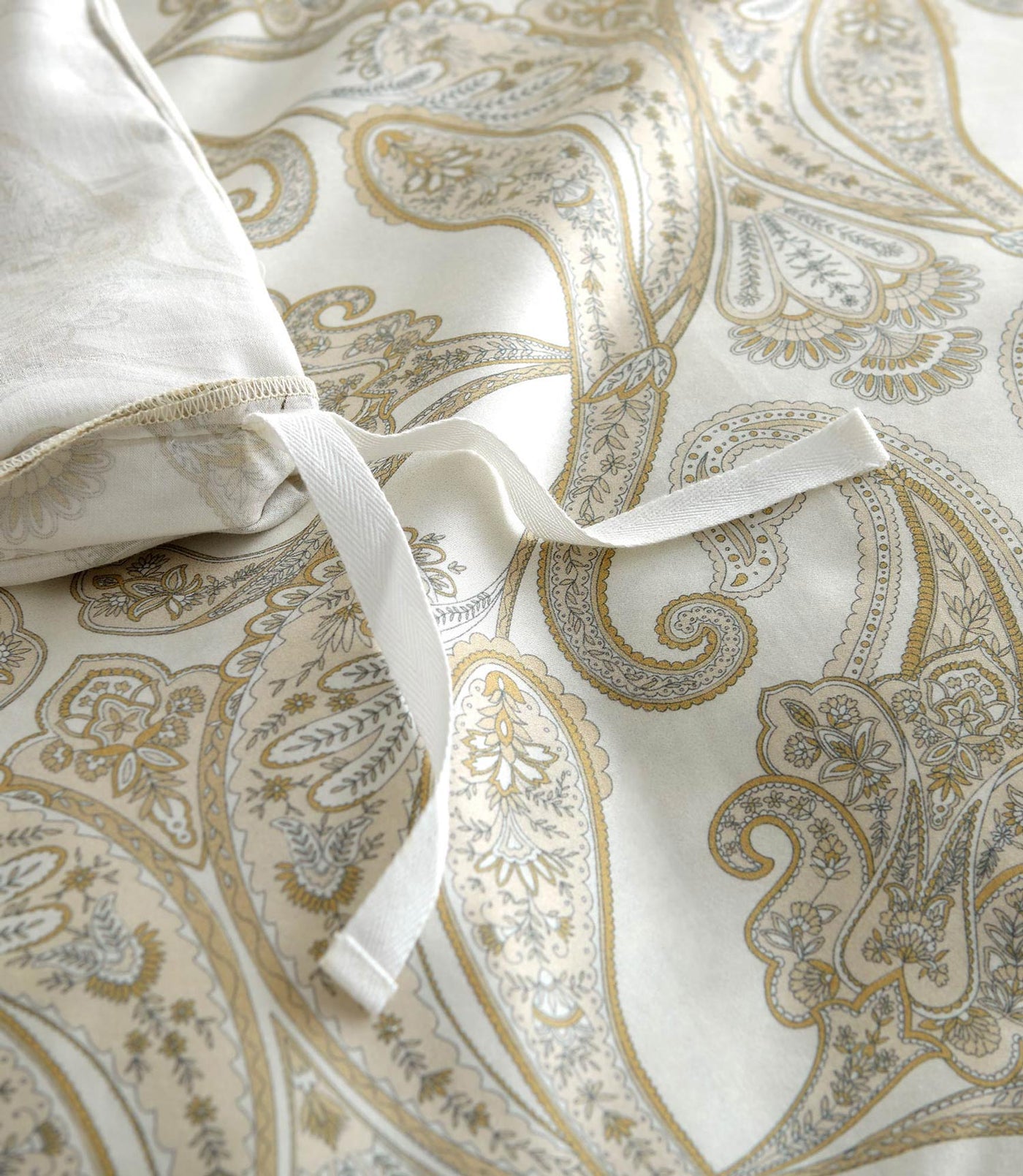 Close-up of ivory cotton duvet cover with gold and silver paisley print and interior tie detail.
