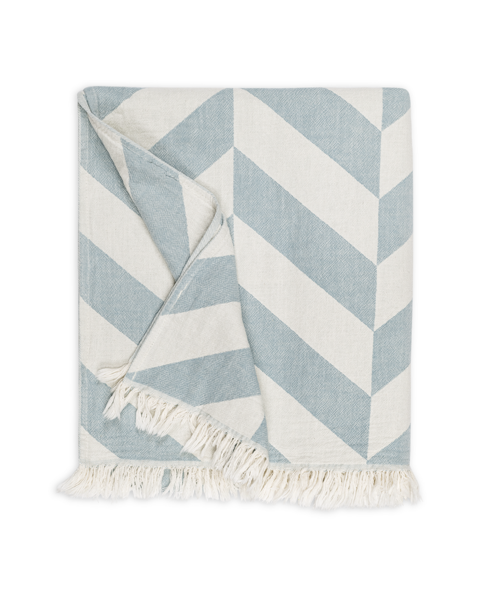 The Paros Beach Towel by Matouk features a blue and white chevron pattern with fringe on one edge, echoing a classic Turkish bath towel, shown on a white background.
