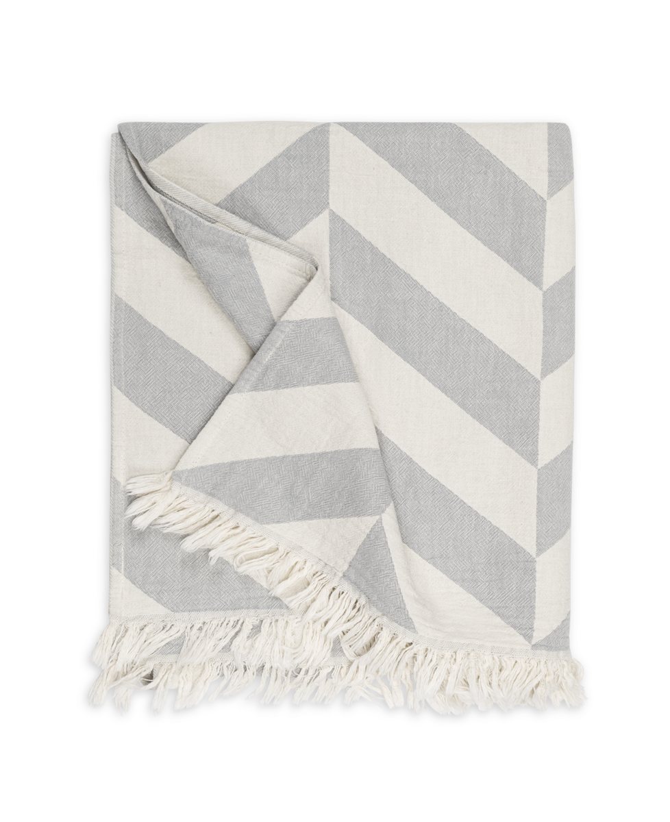 The Paros Beach Towel by Matouk features a gray and white chevron pattern with fringed edges, reminiscent of a classic Turkish bath towel, shown on a plain background.