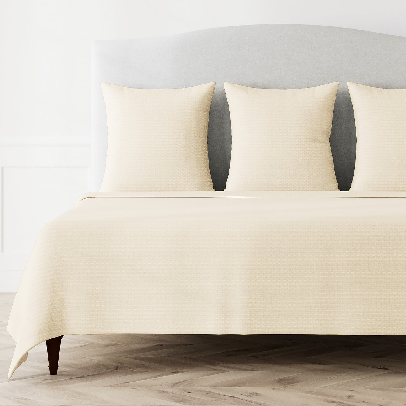 Ivory Ann Gish Pavilion coverlet styled on a bed with matching shams, side angle view.