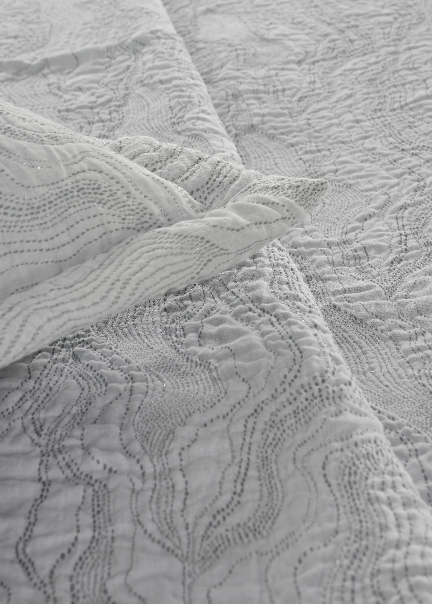 Close-up of Celso de Lemos Perle coverlet showing wave-quilted texture in silver-white cotton.