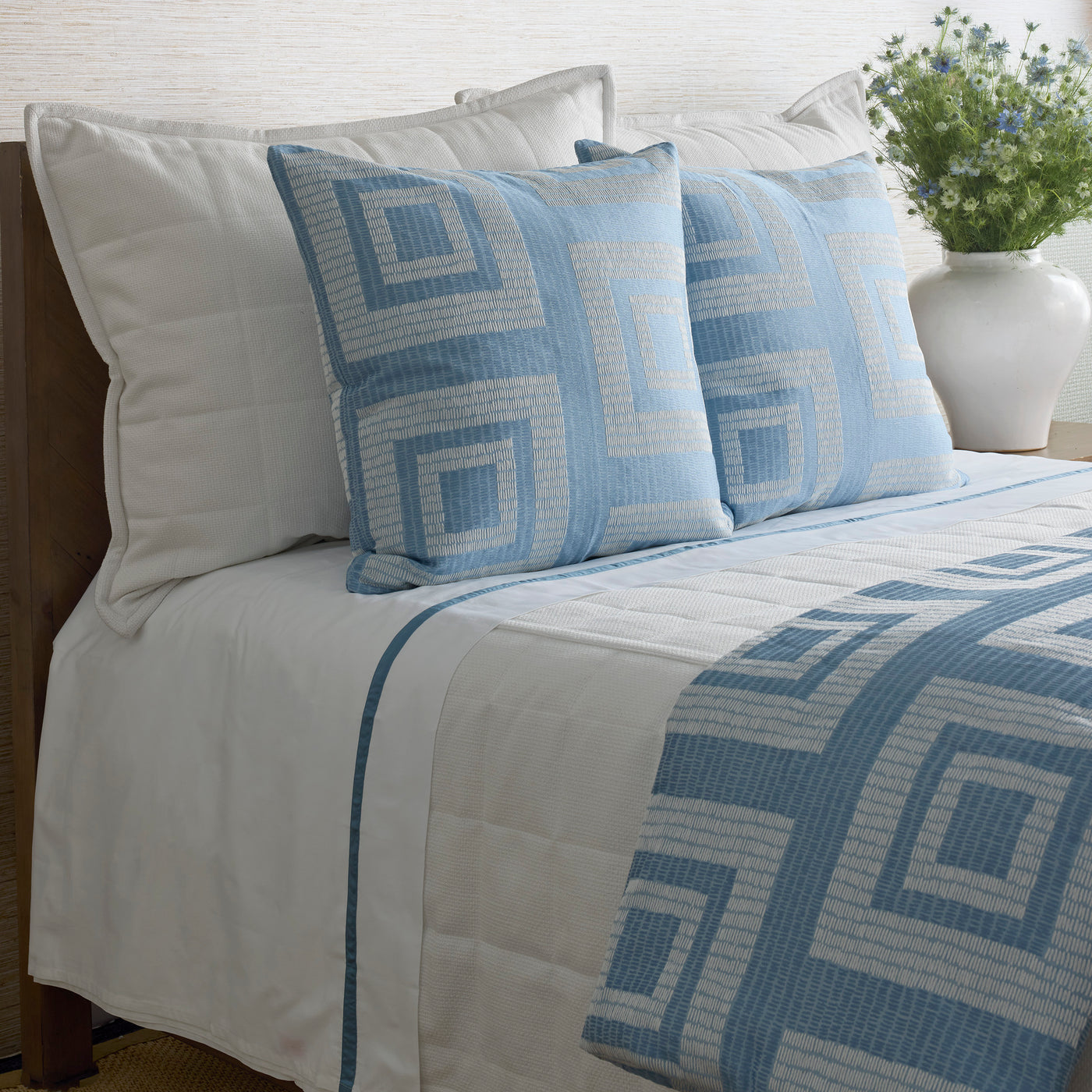 Blue and white geometric Greek key pattern duvet cover and matching shams styled on a made bed.