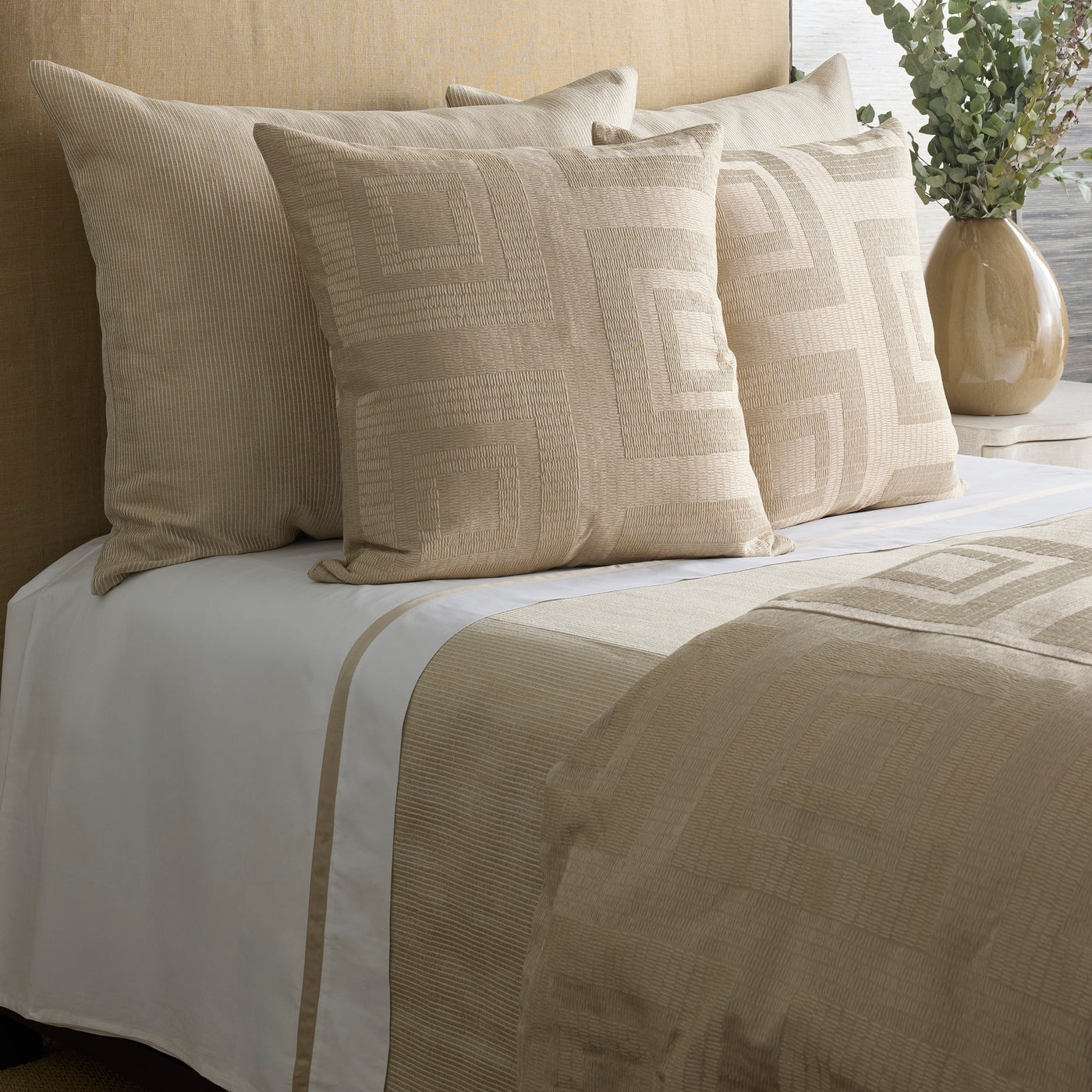 Piastrella duvet and pillows styled on a bed, showing champagne geometric pattern against white sheets.