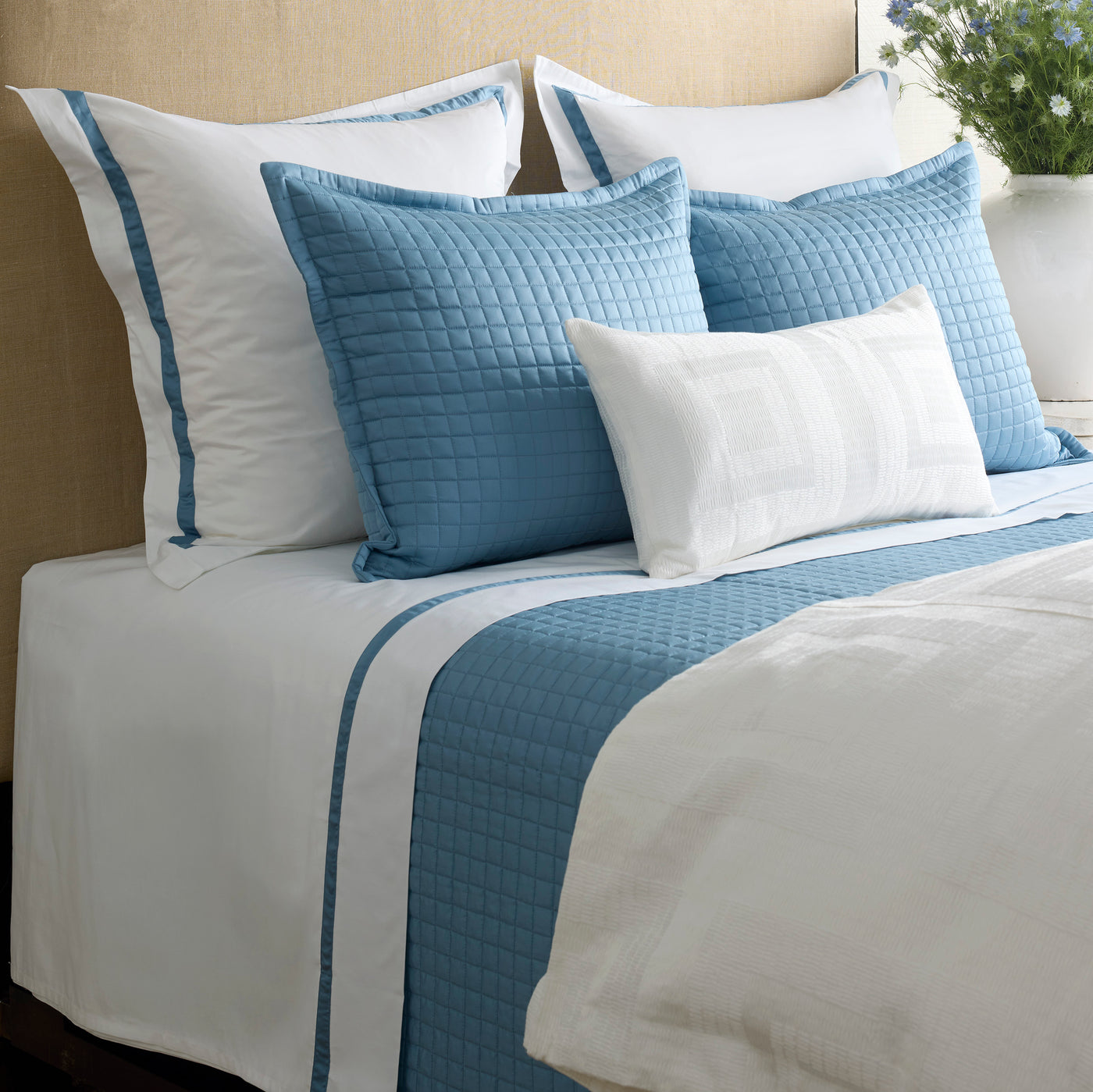 Close-up of Ann Gish Piastrella quilted blue euro shams and bed runner on white bedding.