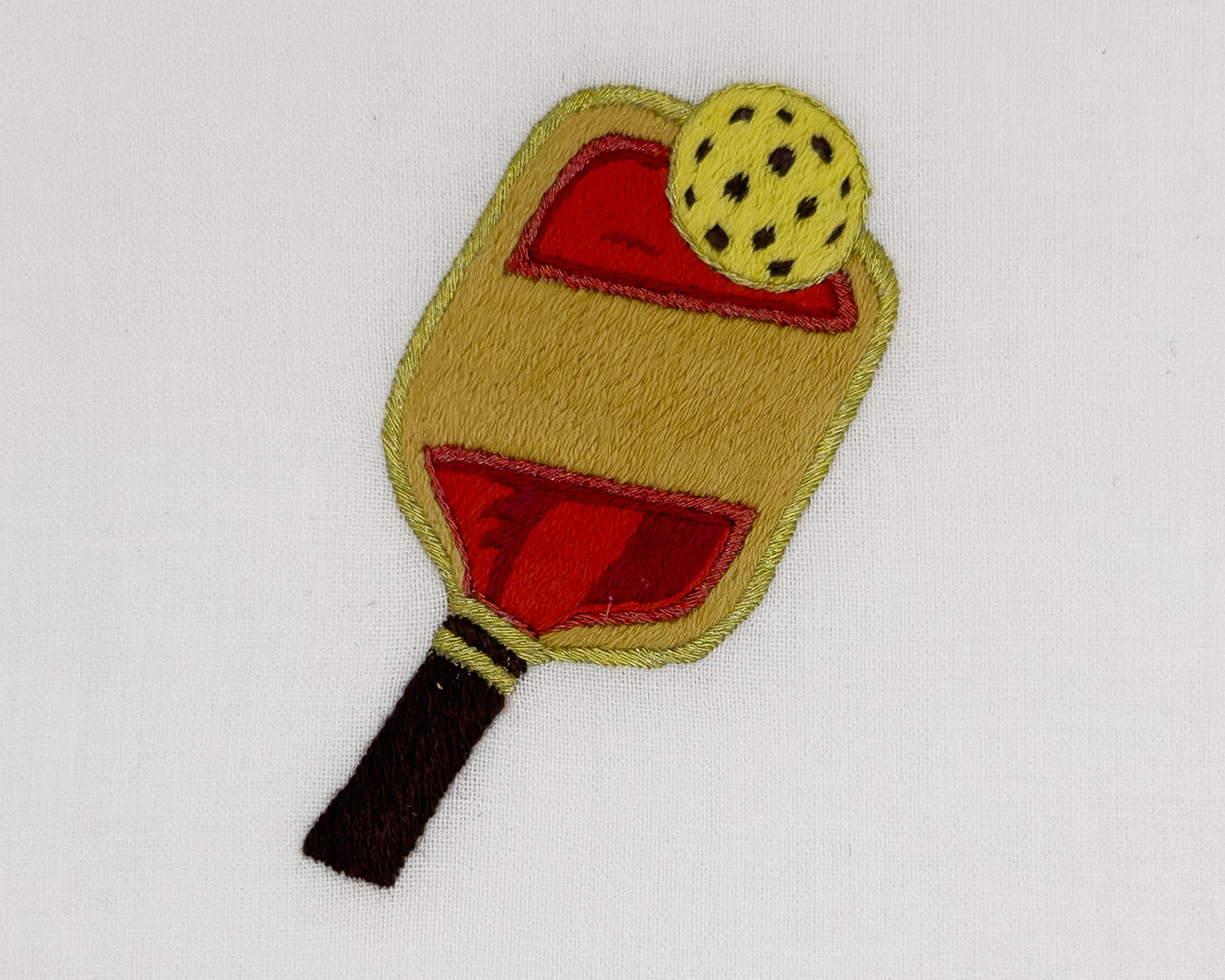 Close-up of embroidered pickleball paddle and ball motif on ivory linen.