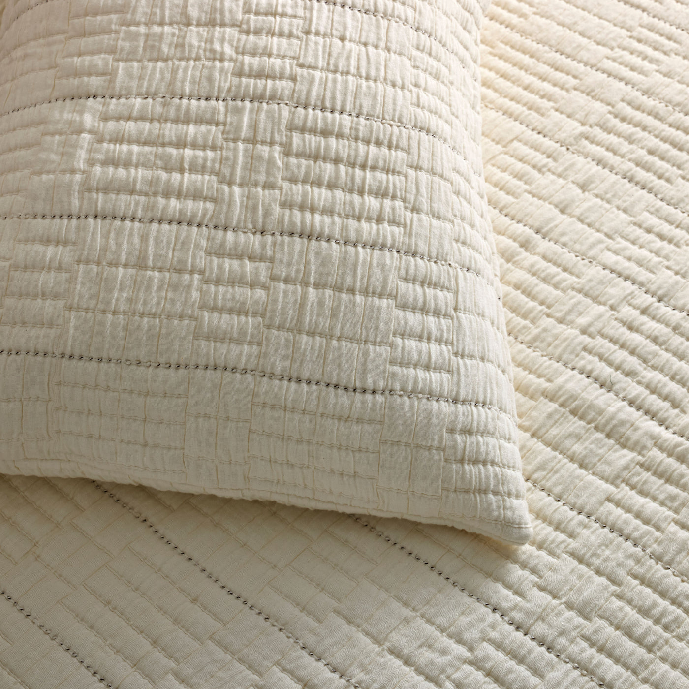 Close-up of ivory quilted pillow sham corner showing pickstitch detail against matching coverlet.
