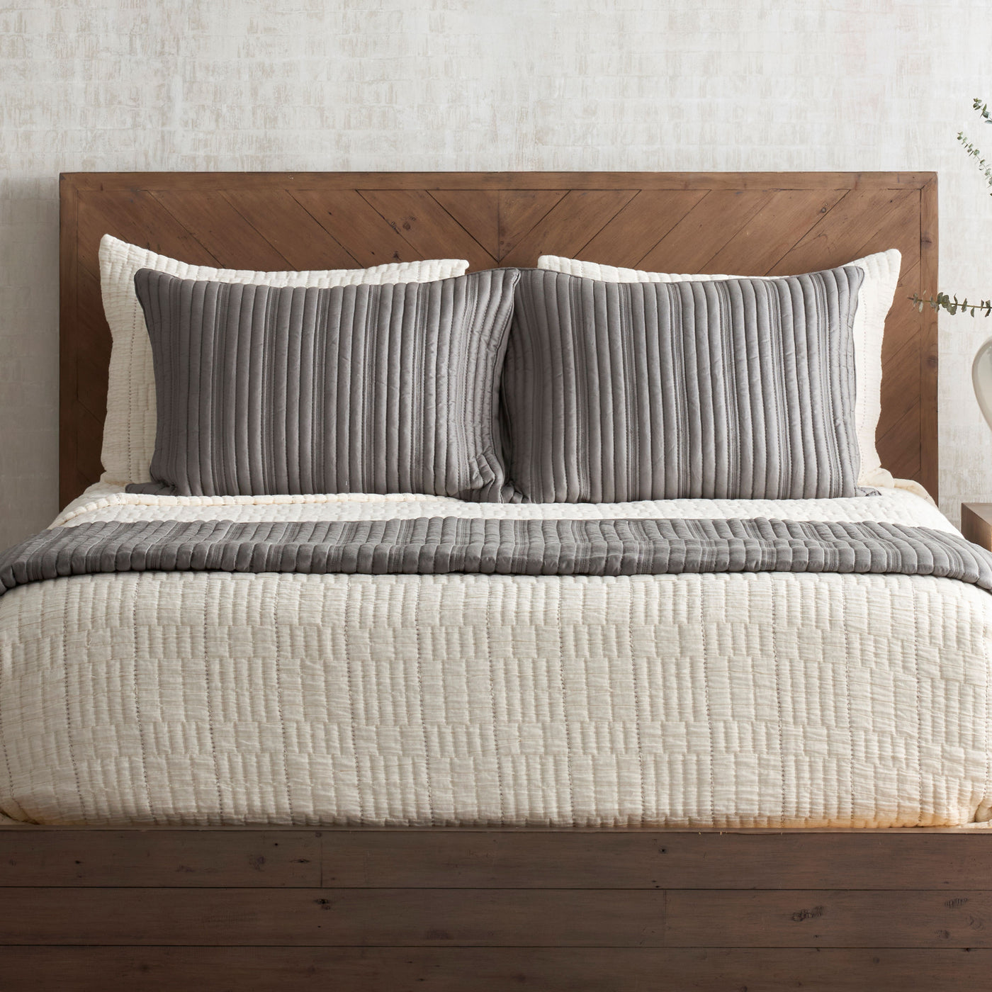 Ivory pickstitch coverlet styled on bed with charcoal striped pillow shams.