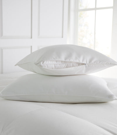 Peacock Alley white pillow protector with zipper closure stacked on pillow atop white bedding.