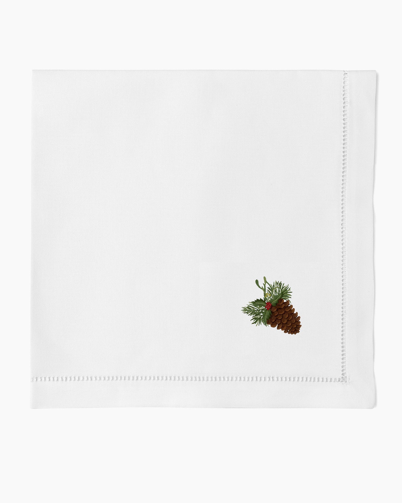 Henry Handwork white linen dinner napkin with embroidered pinecone and holly sprig corner detail.