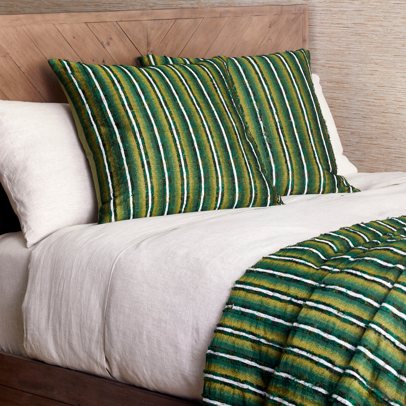 Green and gold striped Ann Gish Pluma pillow shams styled on a bed with white linen bedding.