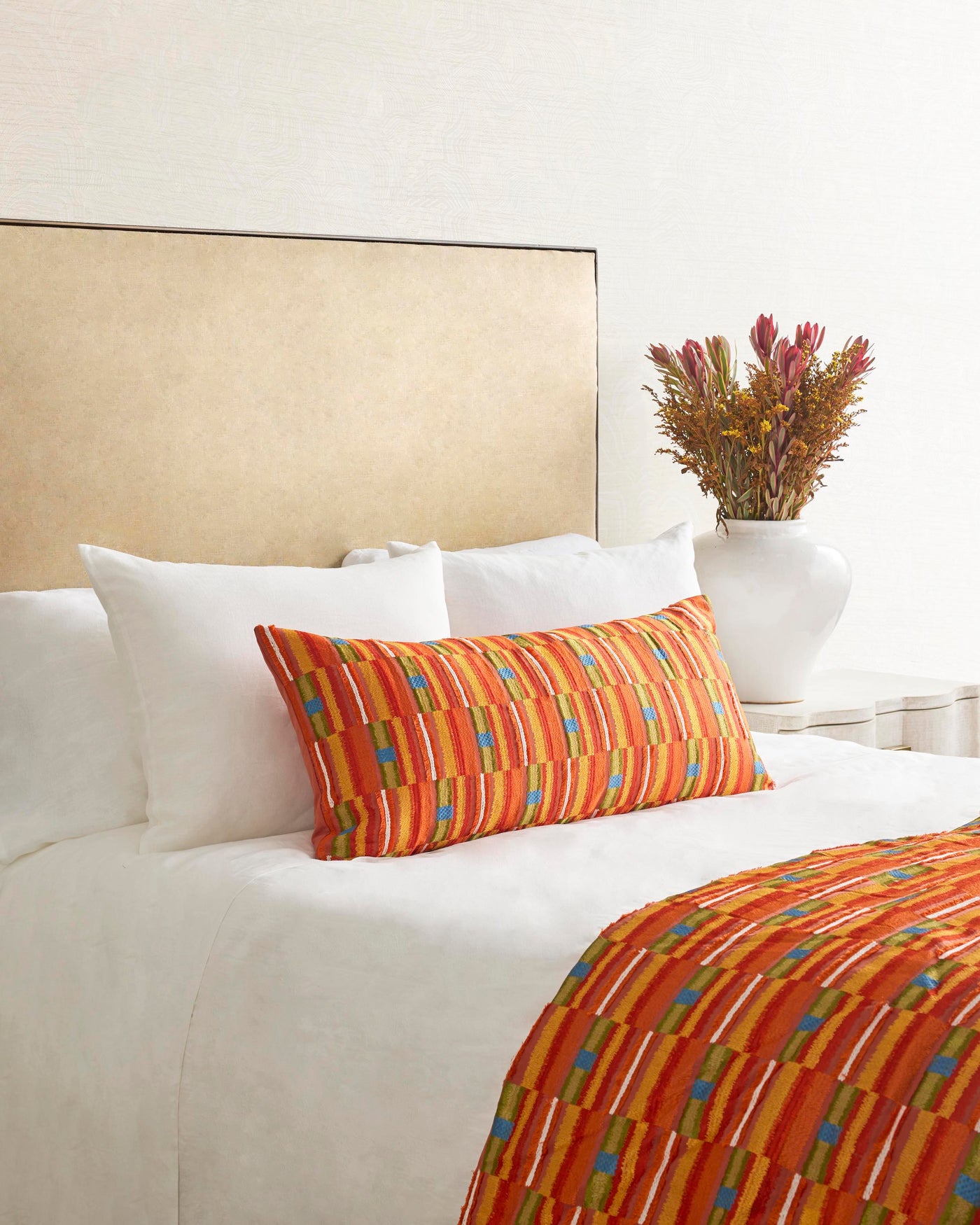 Ann Gish Pluma pillow in tangerine multicolor stripe, styled on white bedding with matching throw.