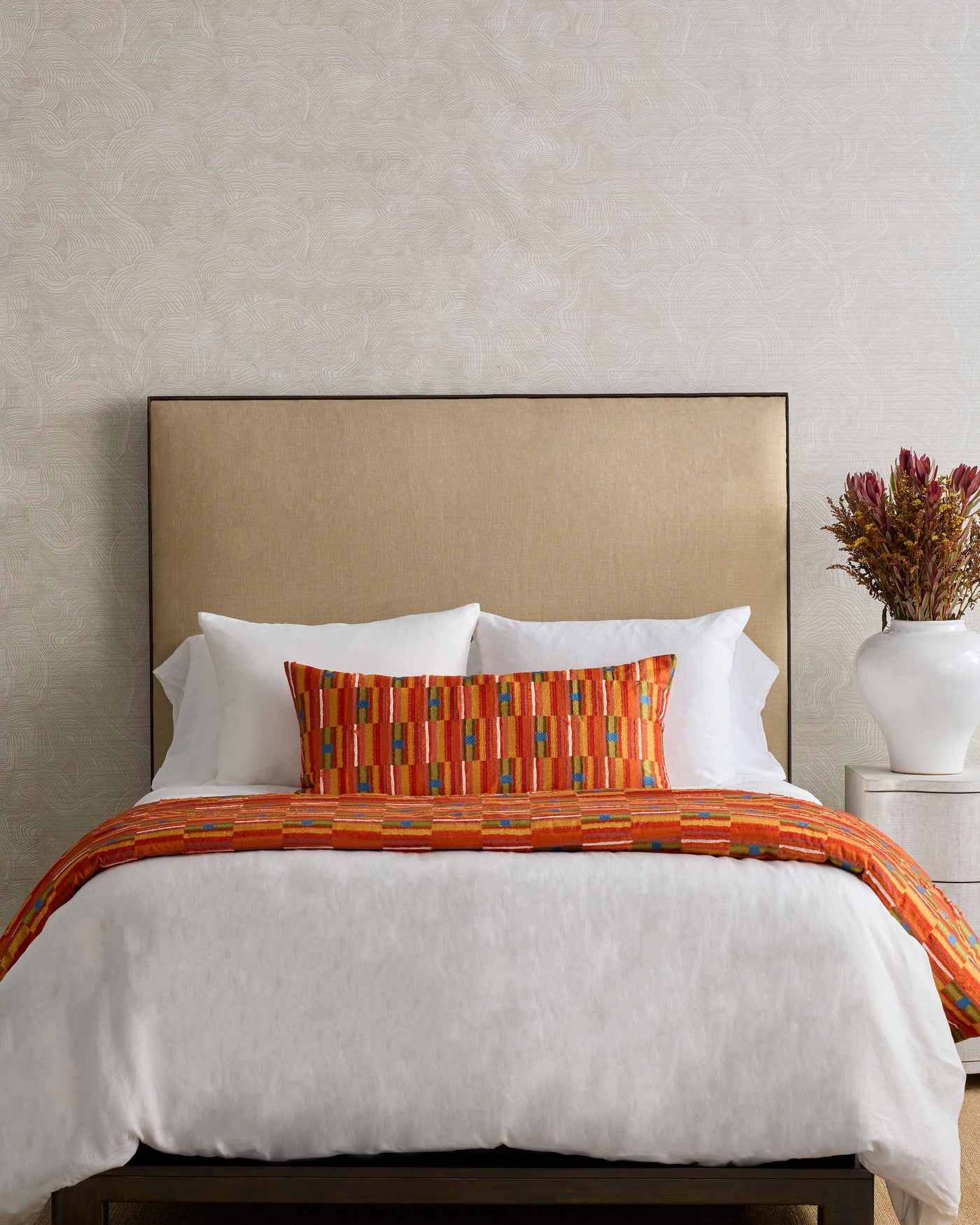 Close-up of Ann Gish Pluma pillow in orange with multicolor geometric stripe pattern on styled bed.