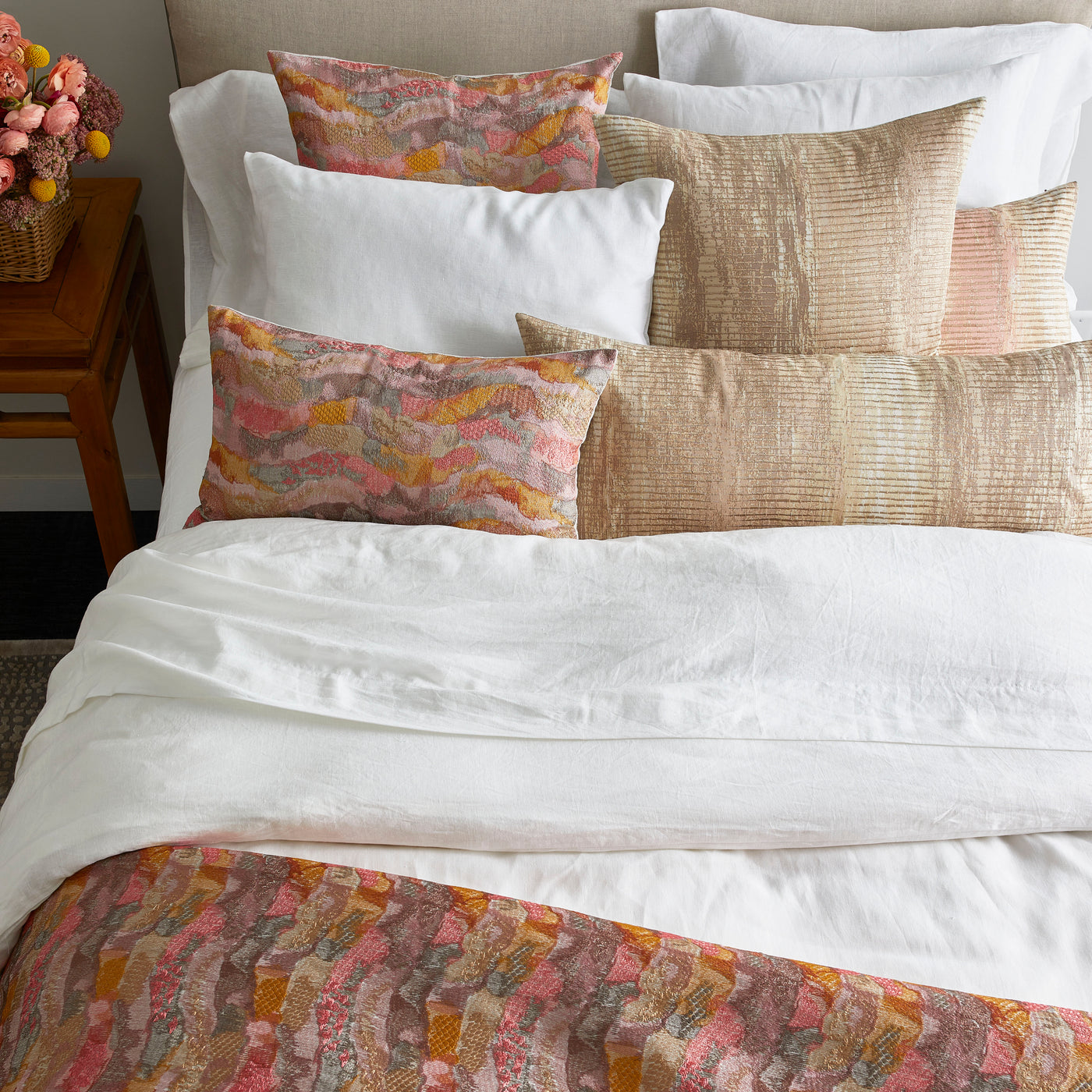 Close-up of Ann Gish Positano pillow with coral and gold wave pattern among white bedding.