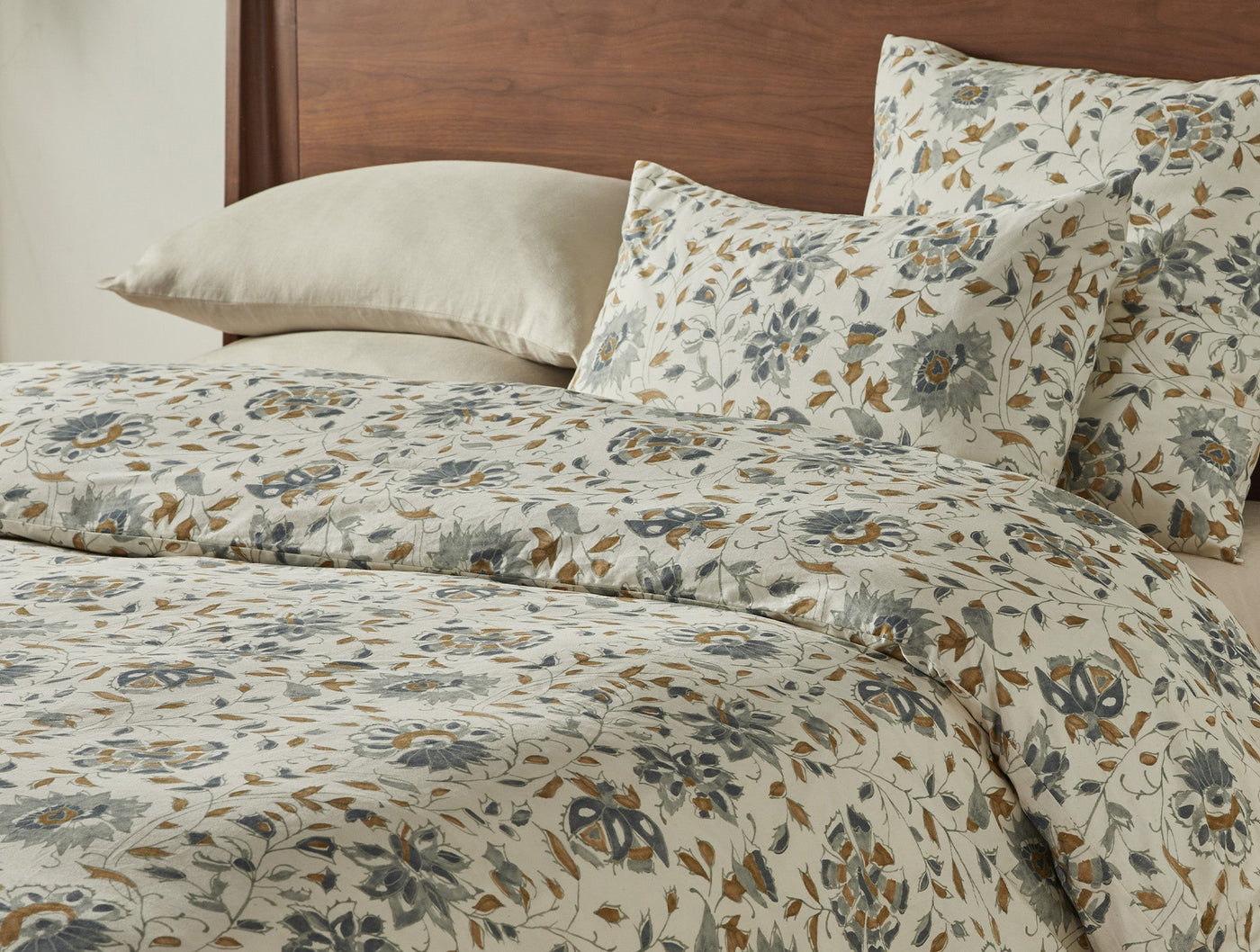 Coyuchi Flora Print sham in ivory with slate and amber botanical print, styled on bed.