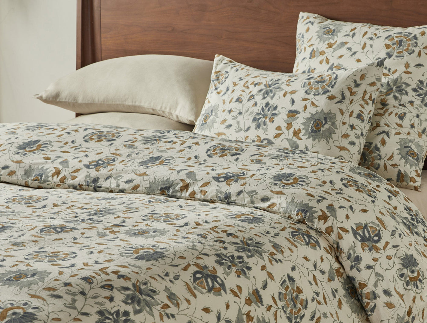 Close-up of Coyuchi Flora Print duvet cover, ivory with blue and amber floral pattern, styled on bed.