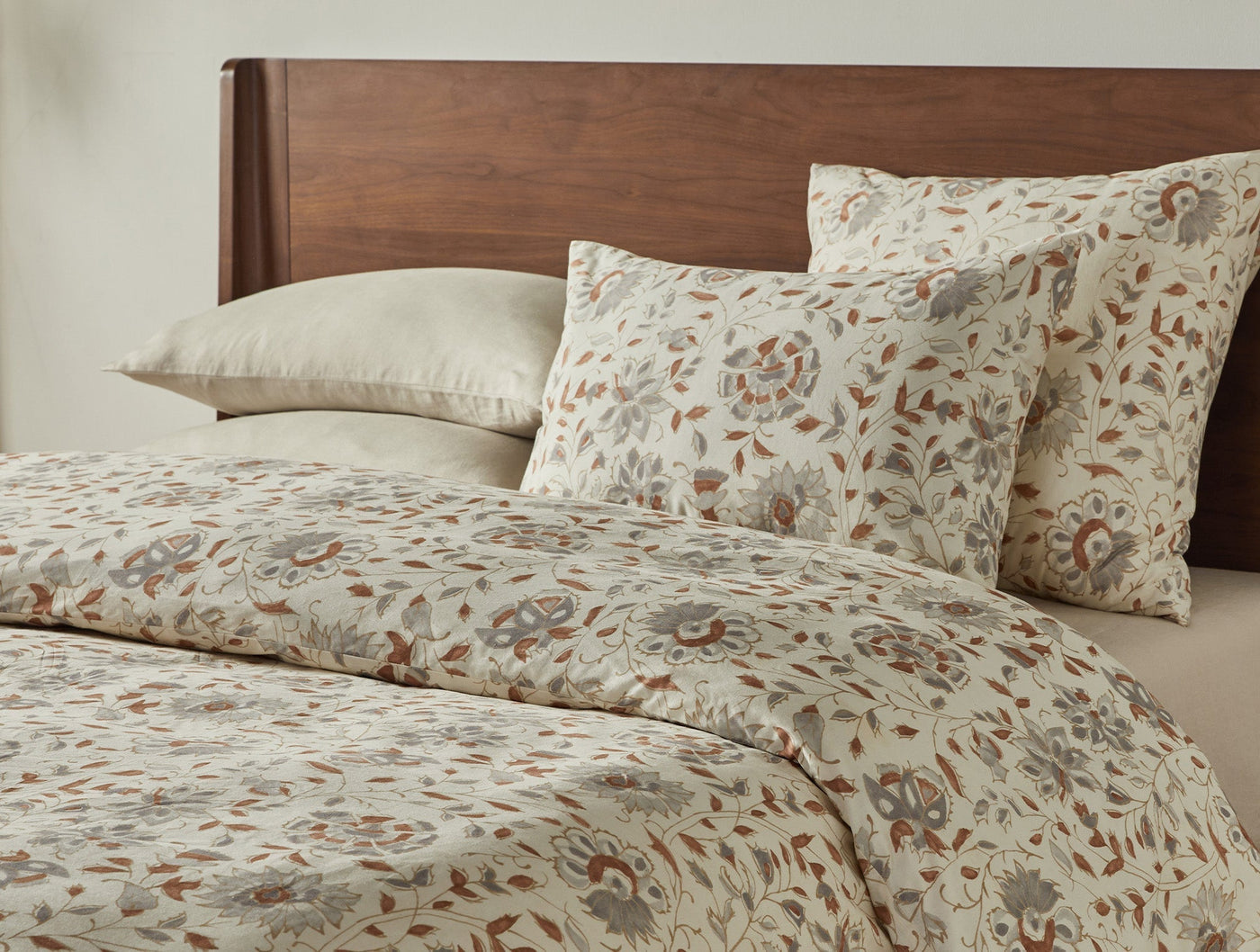Angled view of Coyuchi Flora Print duvet cover and shams, terracotta floral pattern on sage ground.
