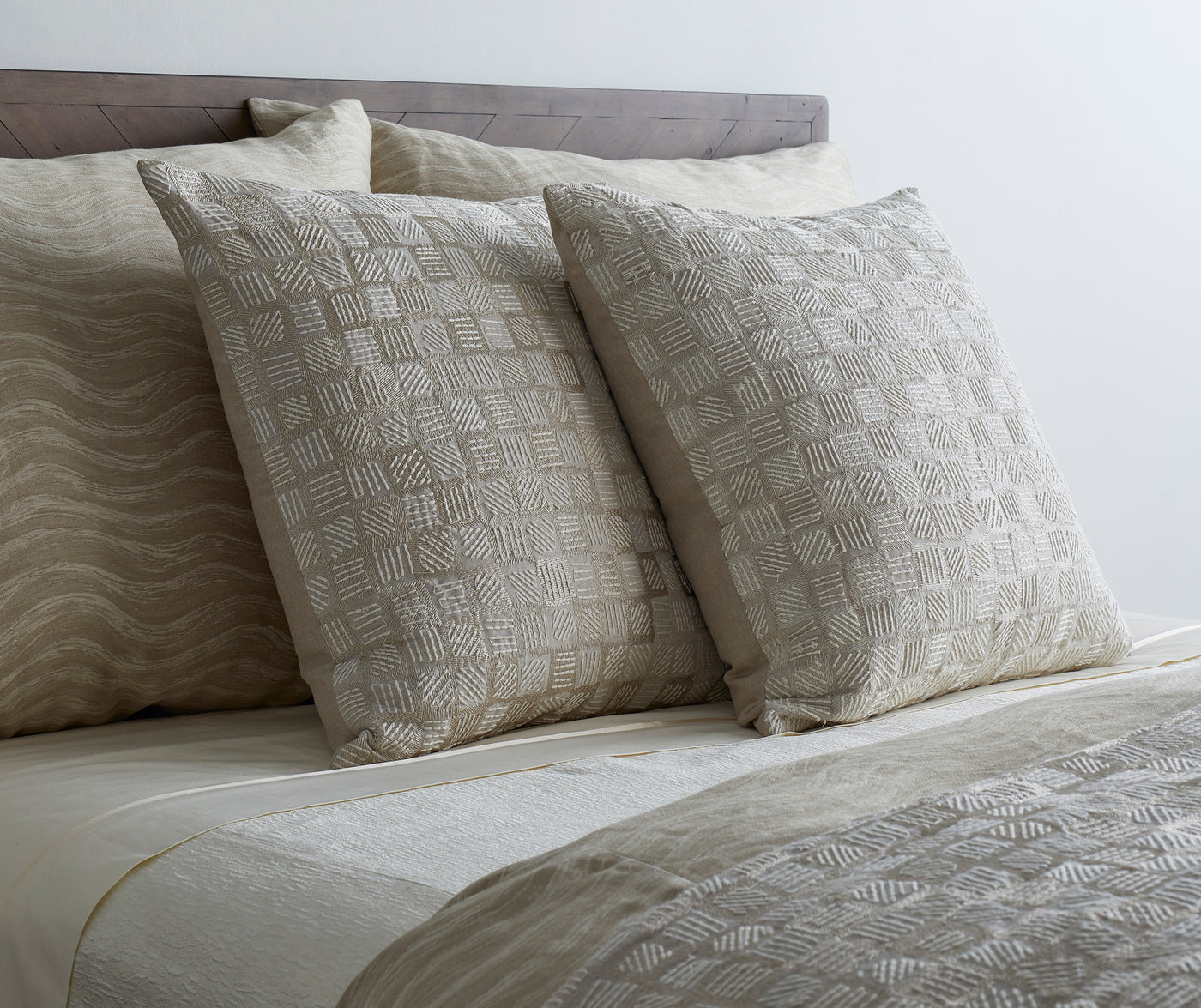 Close-up of Ann Gish Qasaba pillows in ivory and taupe geometric block pattern on styled bed.