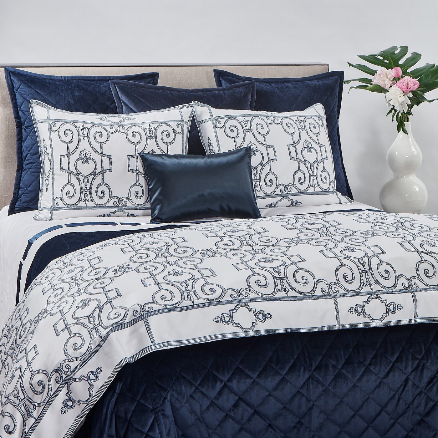 Navy quilted velvet coverlet layered with white embroidered bedding and satin lumbar pillow.