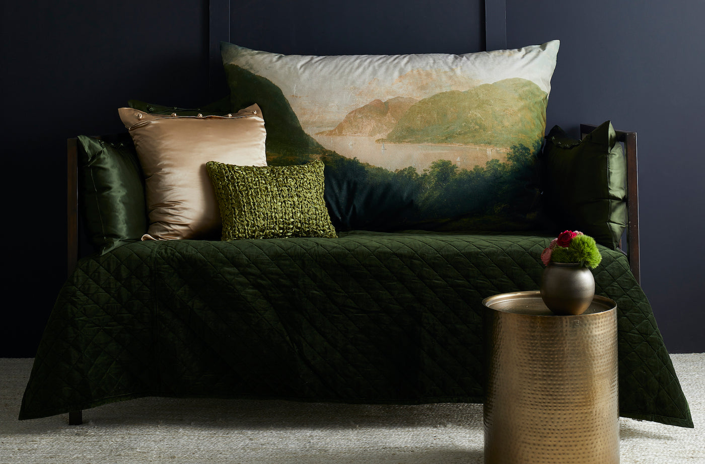 Dark green velvet coverlet draped over a styled bed with mixed decorative pillows.