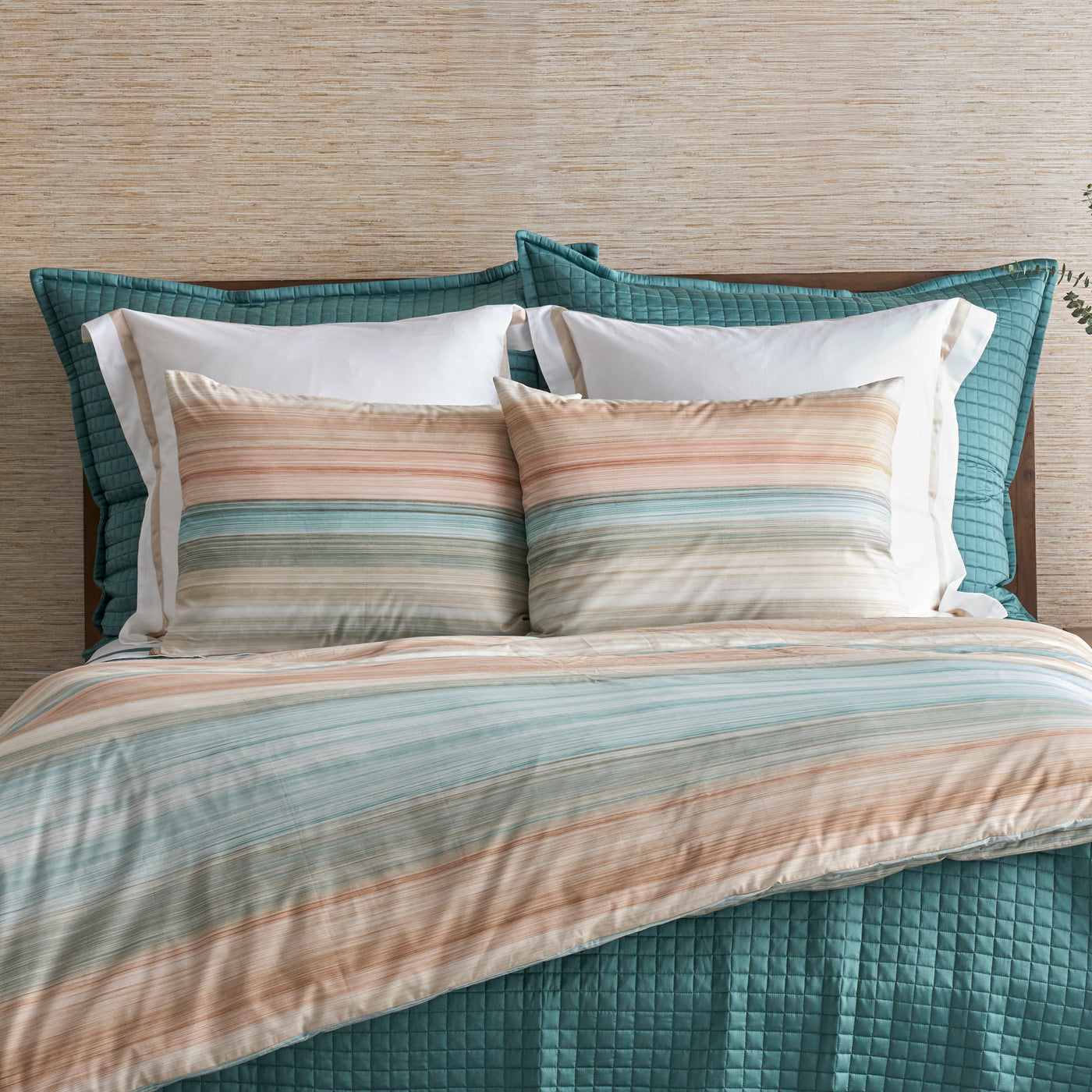 Close-up of a striped cotton sham in teal, blush, and ivory horizontal bands on a styled bed.