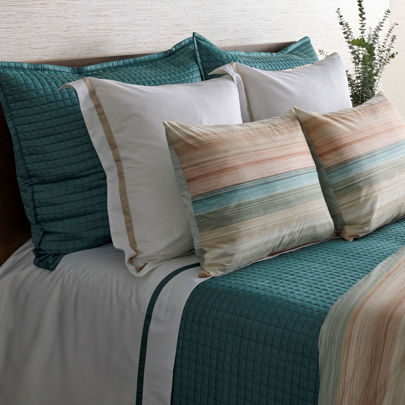 Teal quilted shams layered with striped accent pillows on a styled bed.