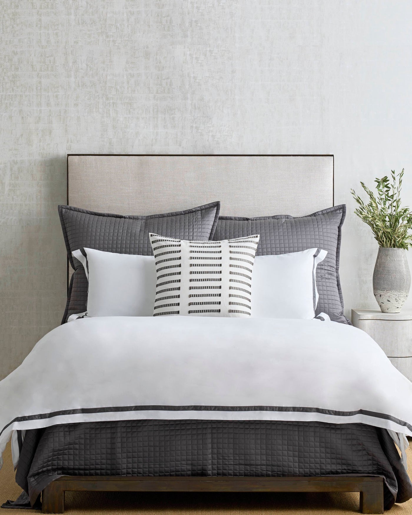 White cotton duvet with charcoal trim, styled with quilted shams and a striped lumbar pillow.