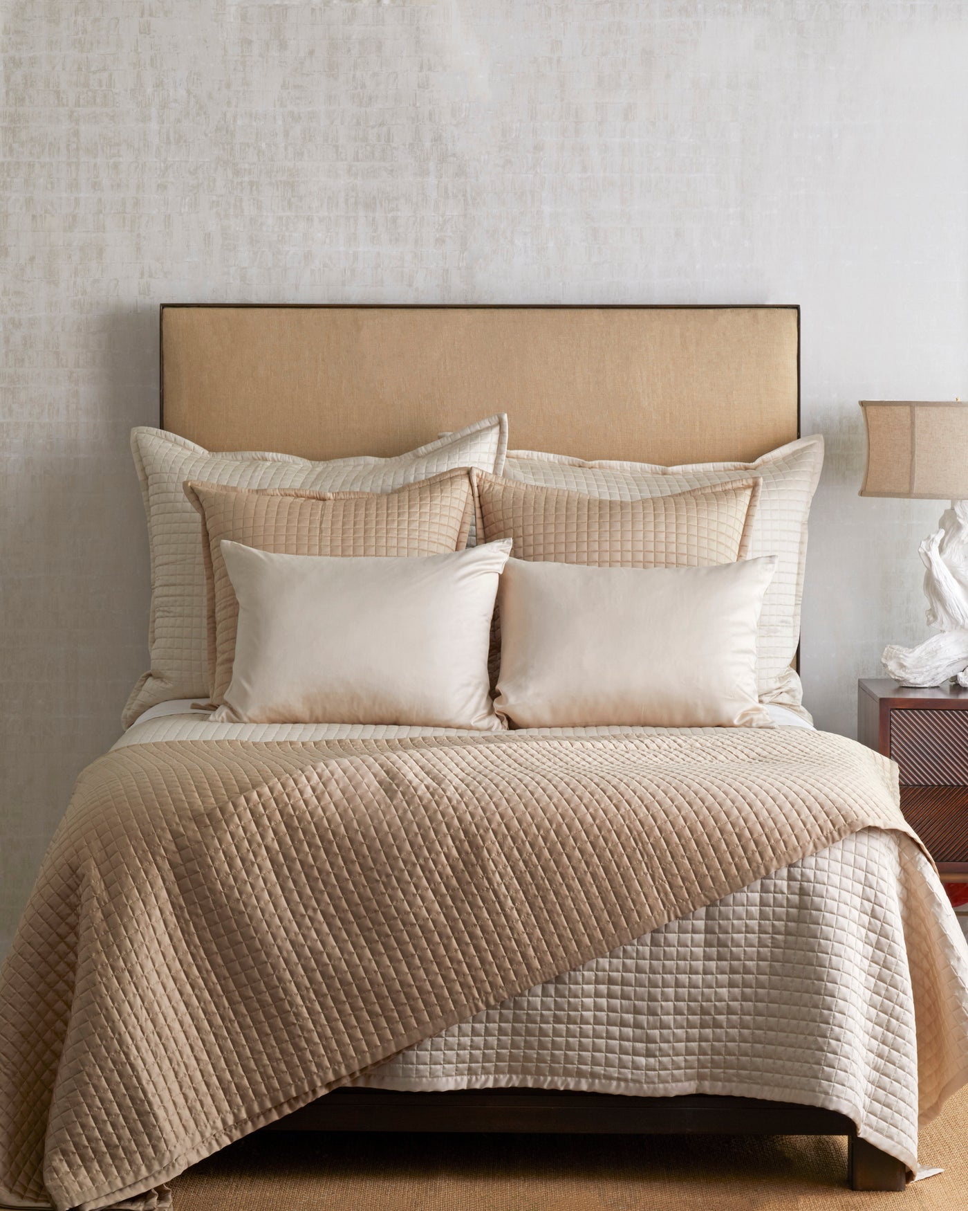 Champagne quilted coverlet layered with ivory pillows on a styled neutral bedroom bed.