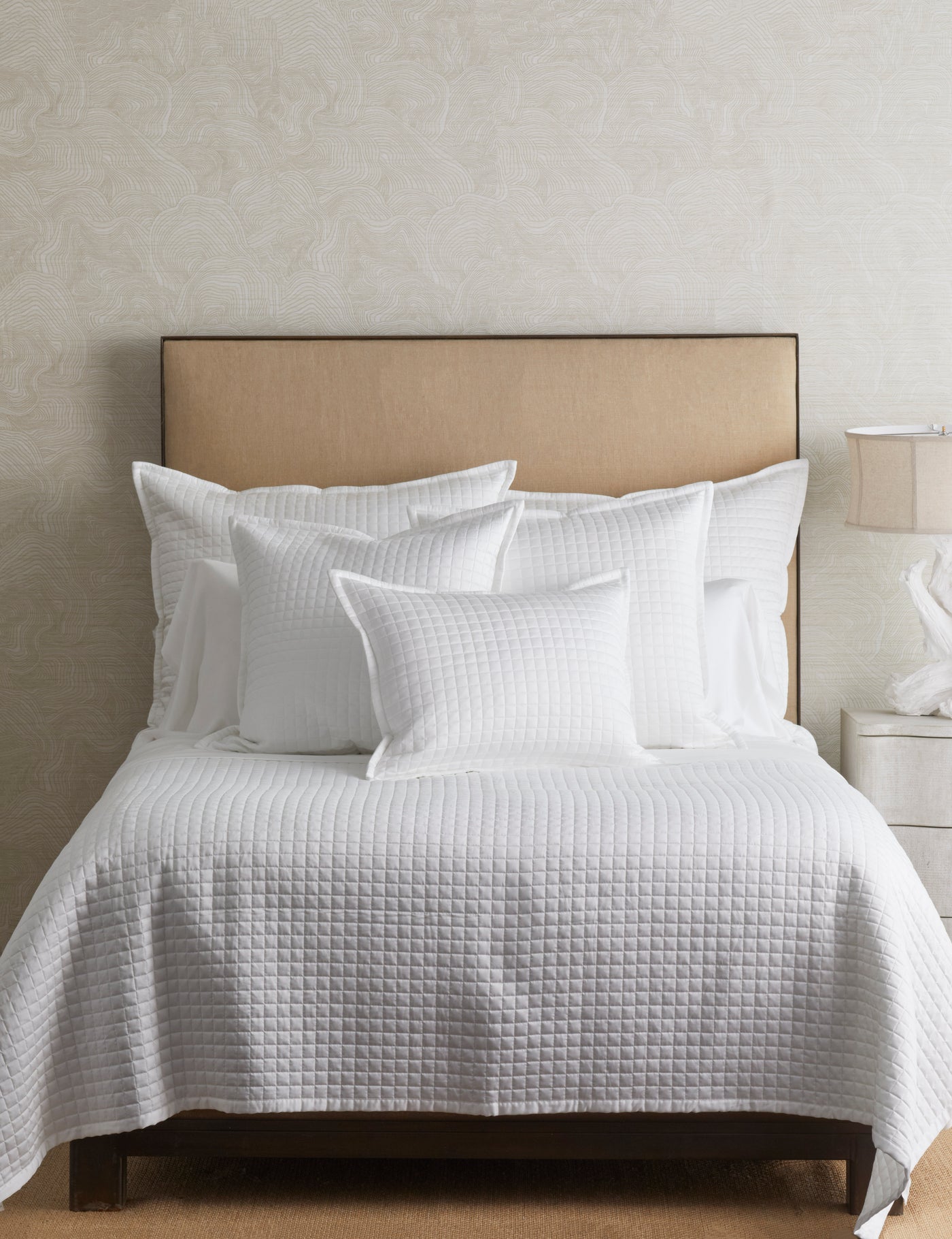 Close-up of white quilted coverlet and layered white pillowcases on a styled bed.
