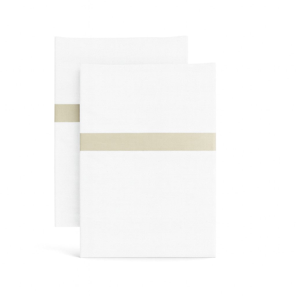 Ann Gish white cotton pillowcases with champagne trim band, folded pair on white background.