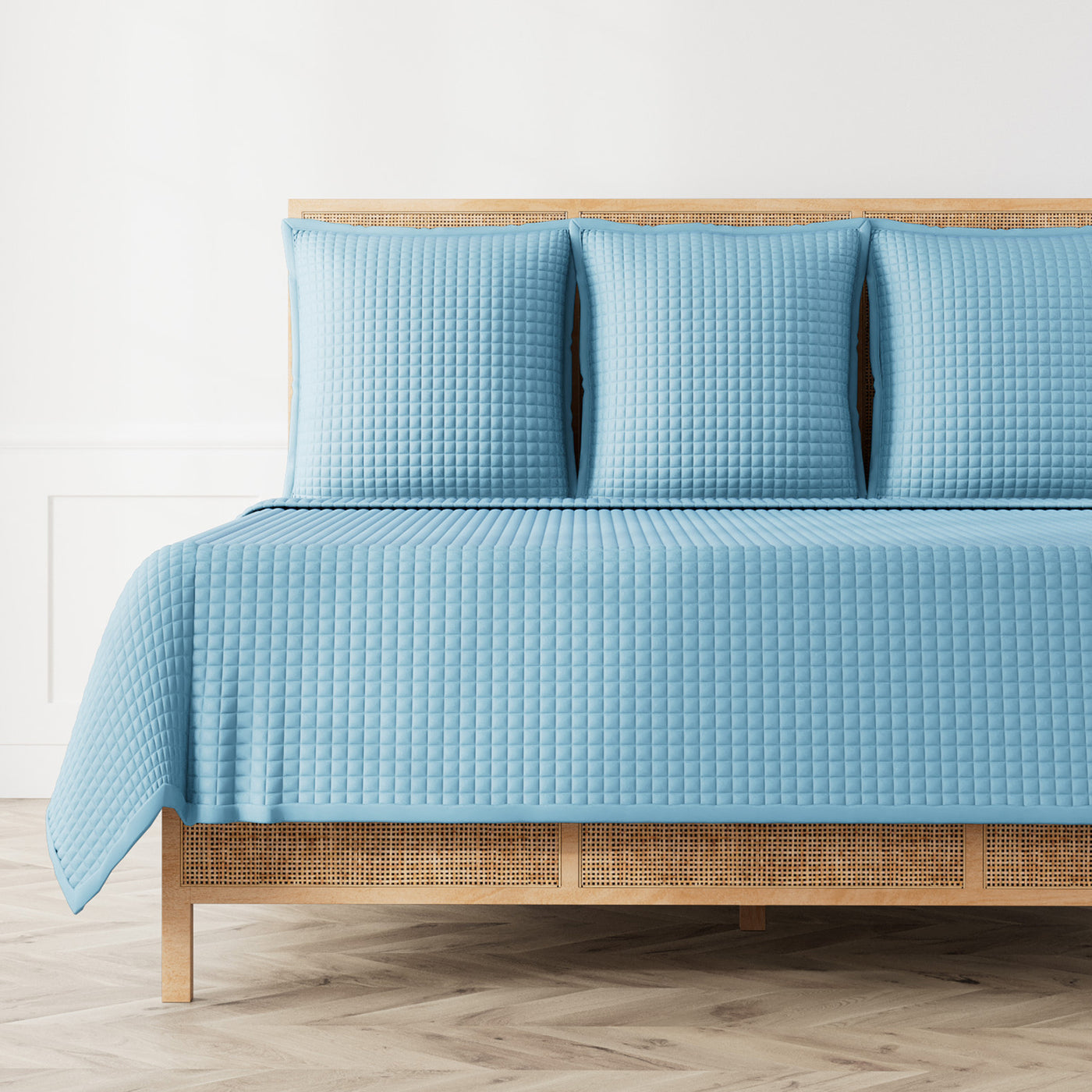 Ann Gish sky blue quilted coverlet and shams styled on a rattan bed frame.