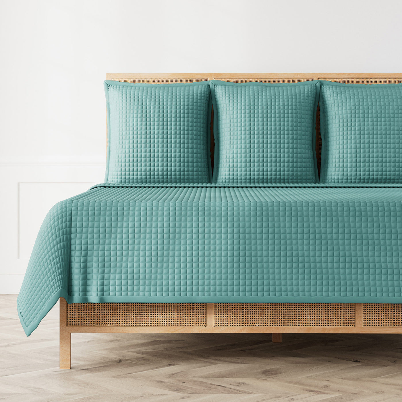 Teal quilted coverlet with waffle texture draped over rattan bed with matching shams.