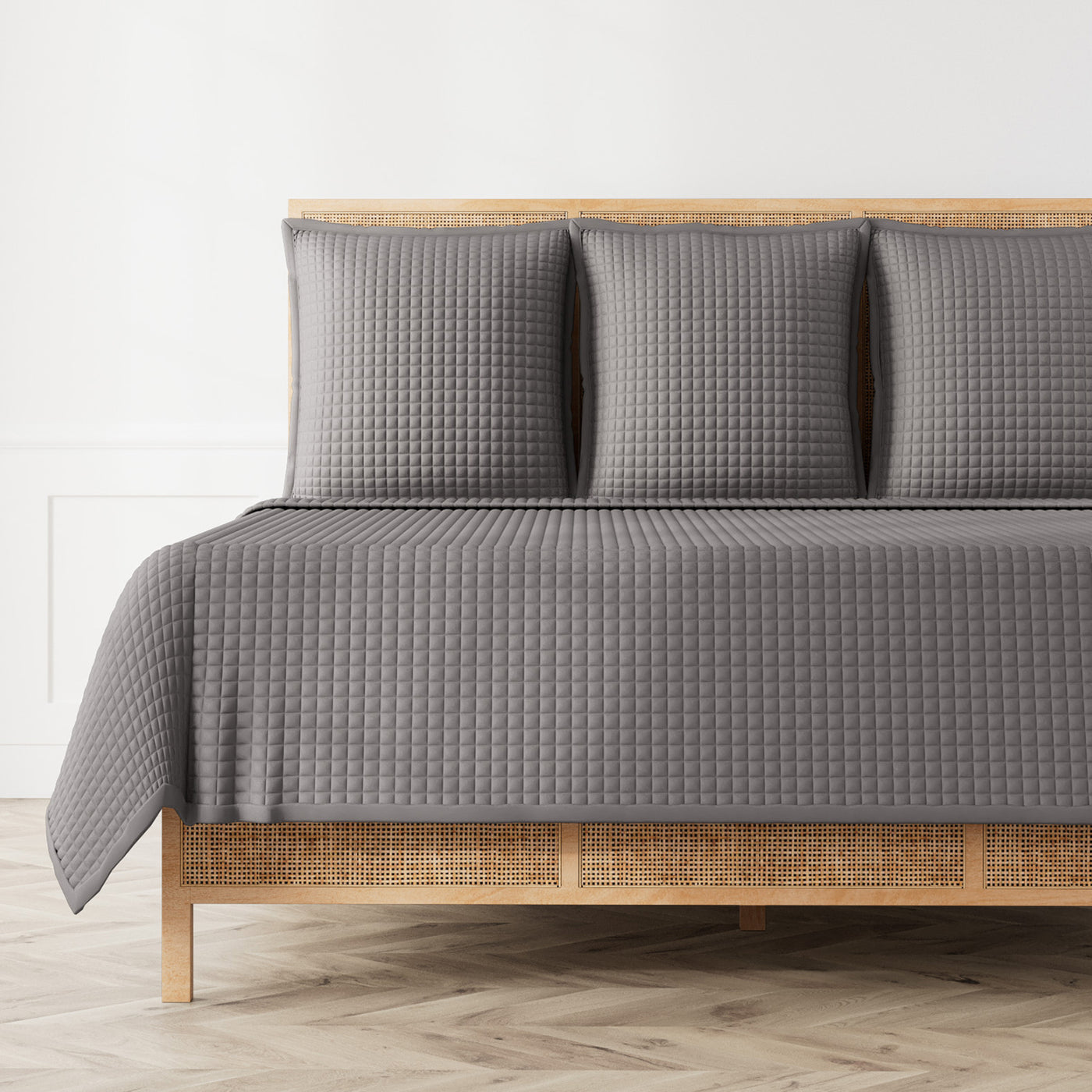 Ann Gish slate quilted coverlet with waffle texture, styled on rattan bed with matching shams.